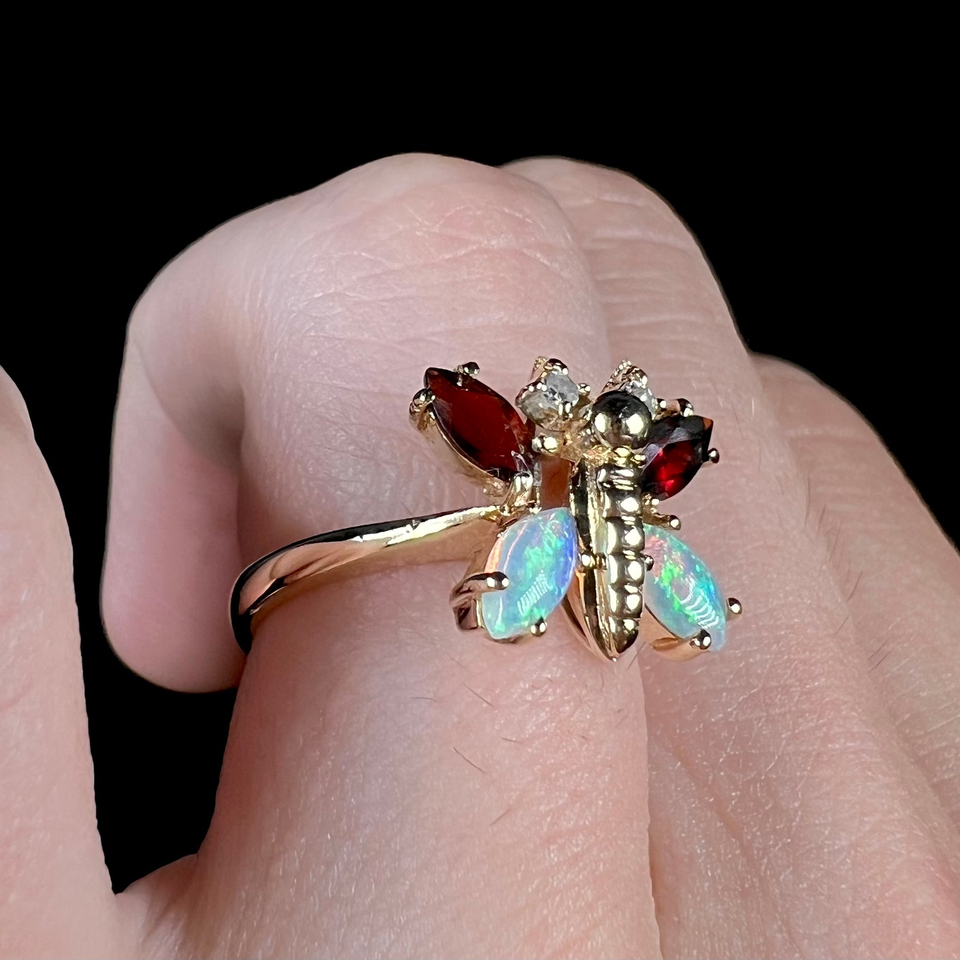 A yellow gold butterfly ring mounted with marquise cut garnets and opals and round diamond accents.