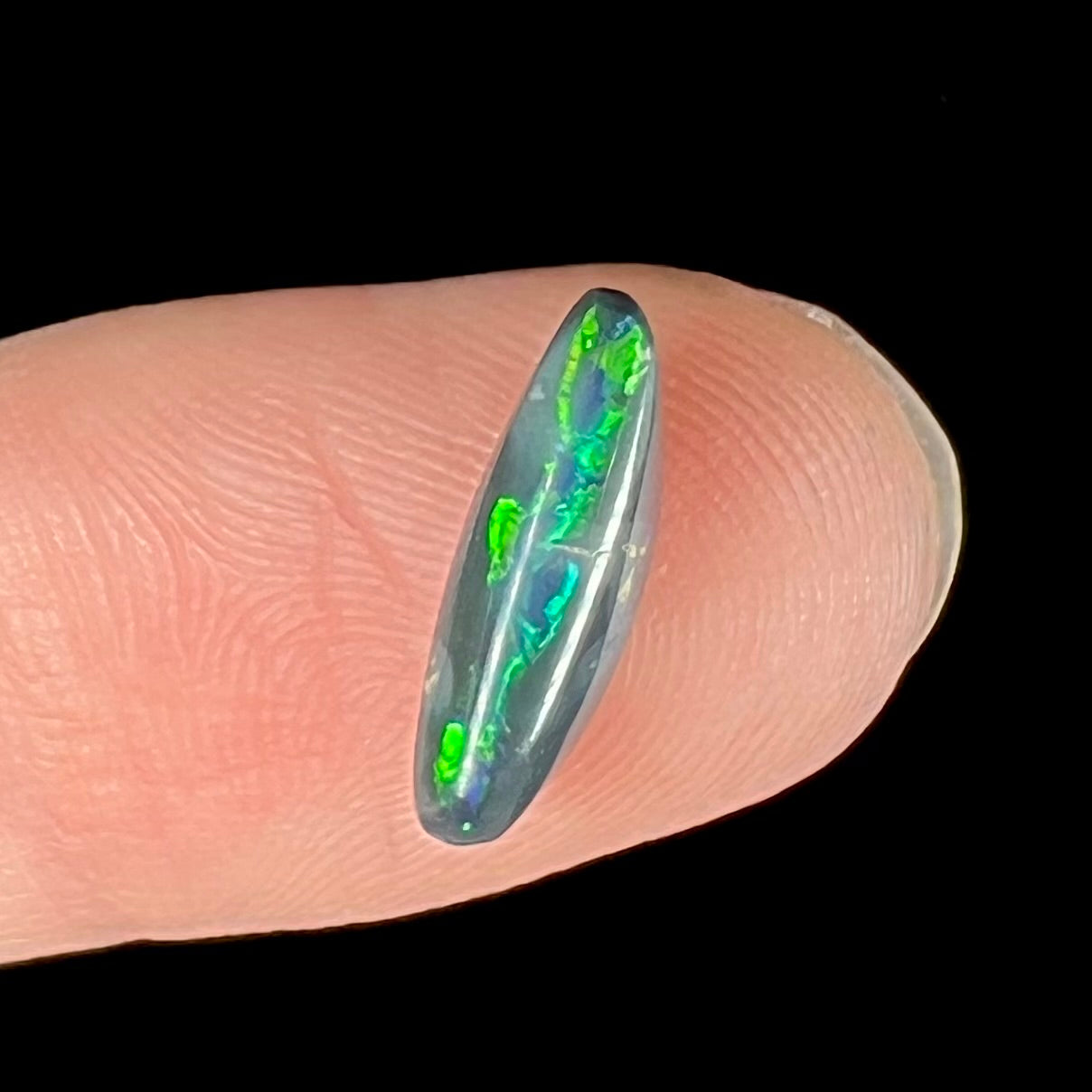 A loose, elongated oval cut black opal that has a green and blue cat's eye.