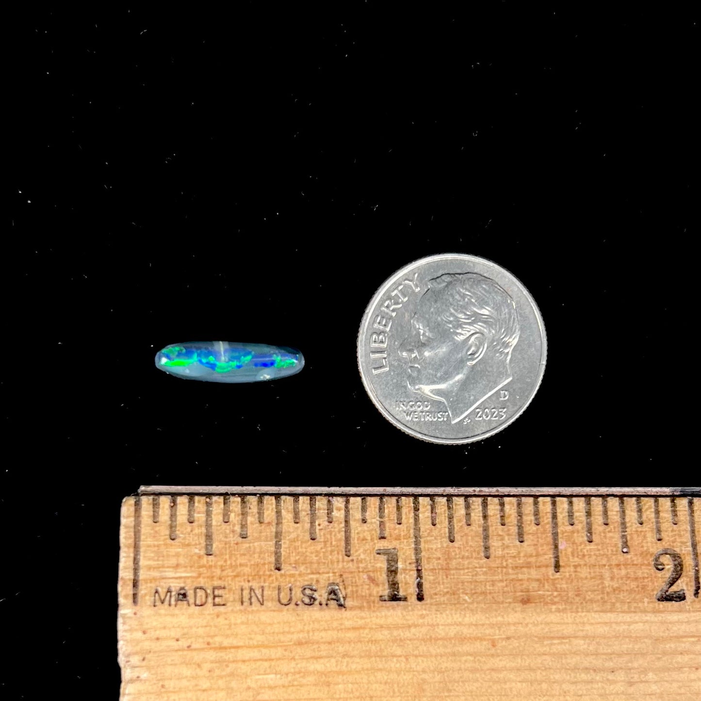 A loose, elongated oval cut black opal that has a green and blue cat's eye.