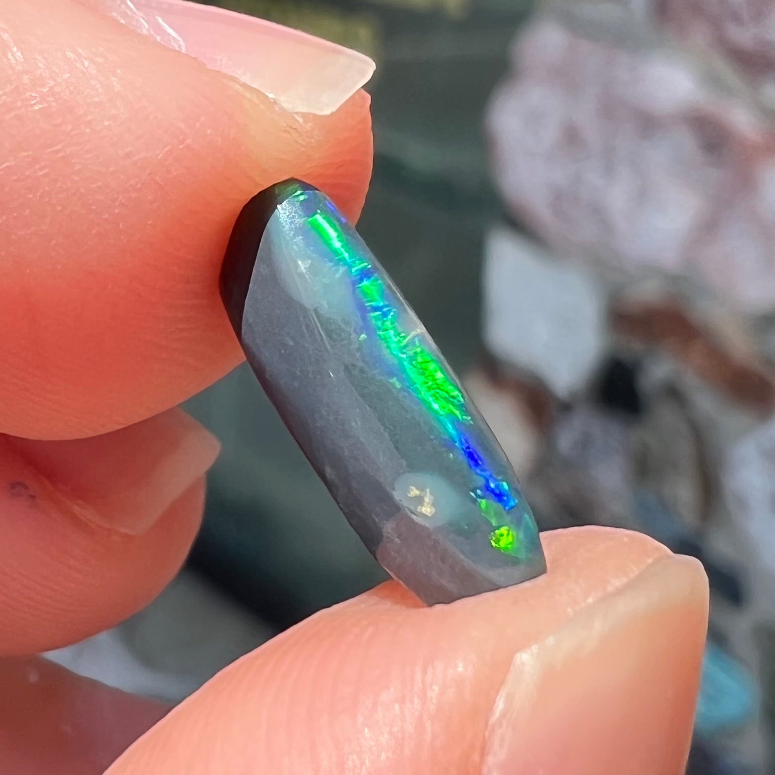 A loose, elongated oval cut black opal that has a green and blue cat's eye.