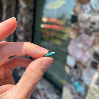 A loose, elongated oval cut black opal that has a green and blue cat's eye.