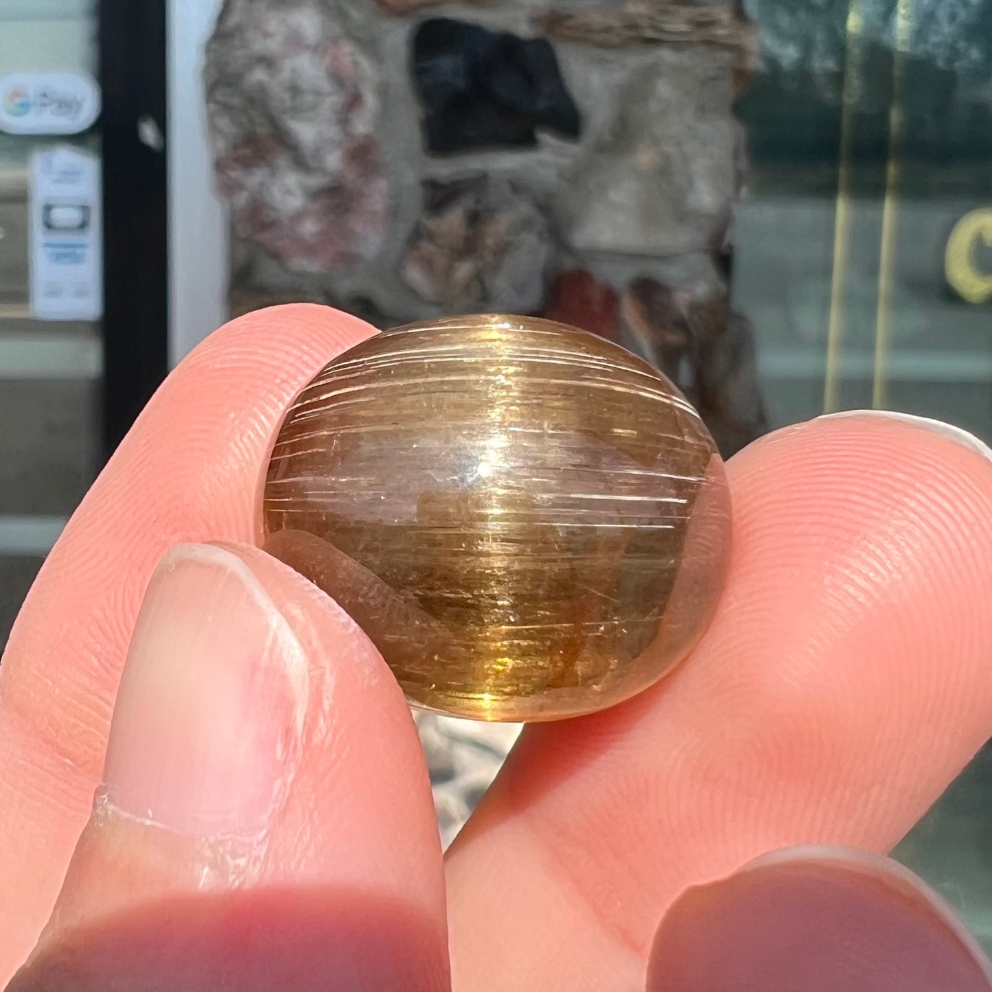 A loose, golden brown cat's eye dravite tourmaline gemstone.  The stone is cut into an oval shaped cabochon.