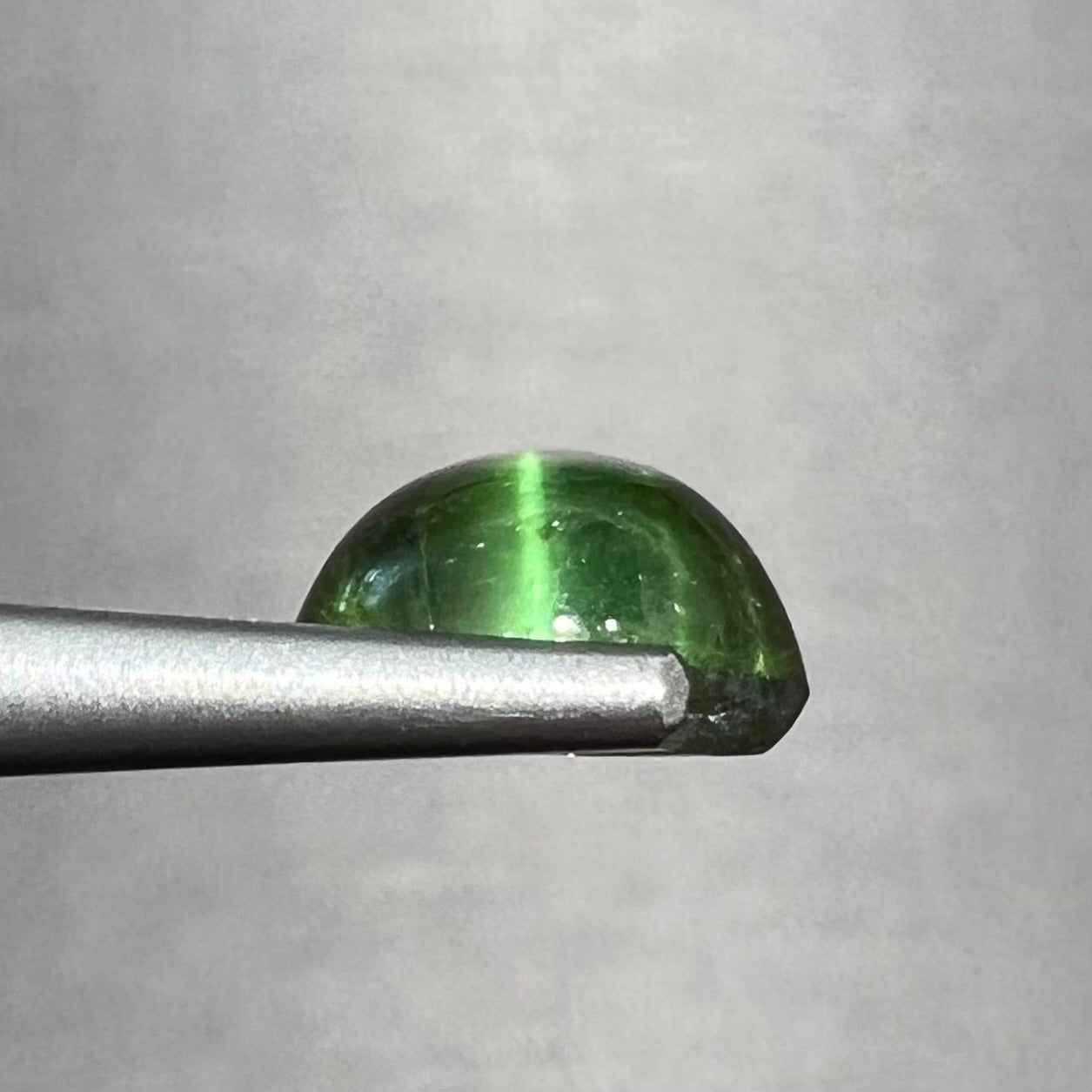 A loose, round cabochon cut green tourmaline stone that displays a cat's eye phenomenon.