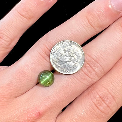 A loose, round cabochon cut green tourmaline stone that displays a cat's eye phenomenon.