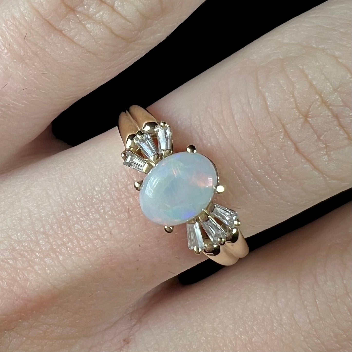 A yellow gold ring set with a natural Australian opal and tapered baguette cut cubic zirconia accents.