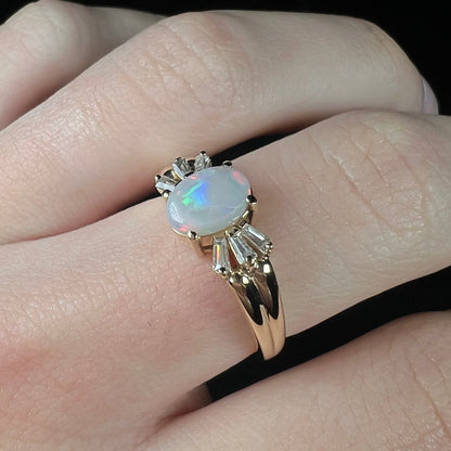 A yellow gold ring set with a natural Australian opal and tapered baguette cut cubic zirconia accents.