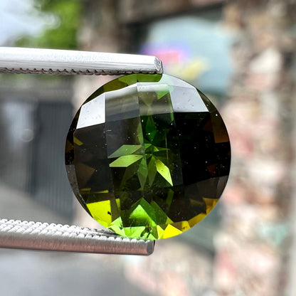 A loose, round checkerboard cut green tourmaline stone with flashes of yellow.