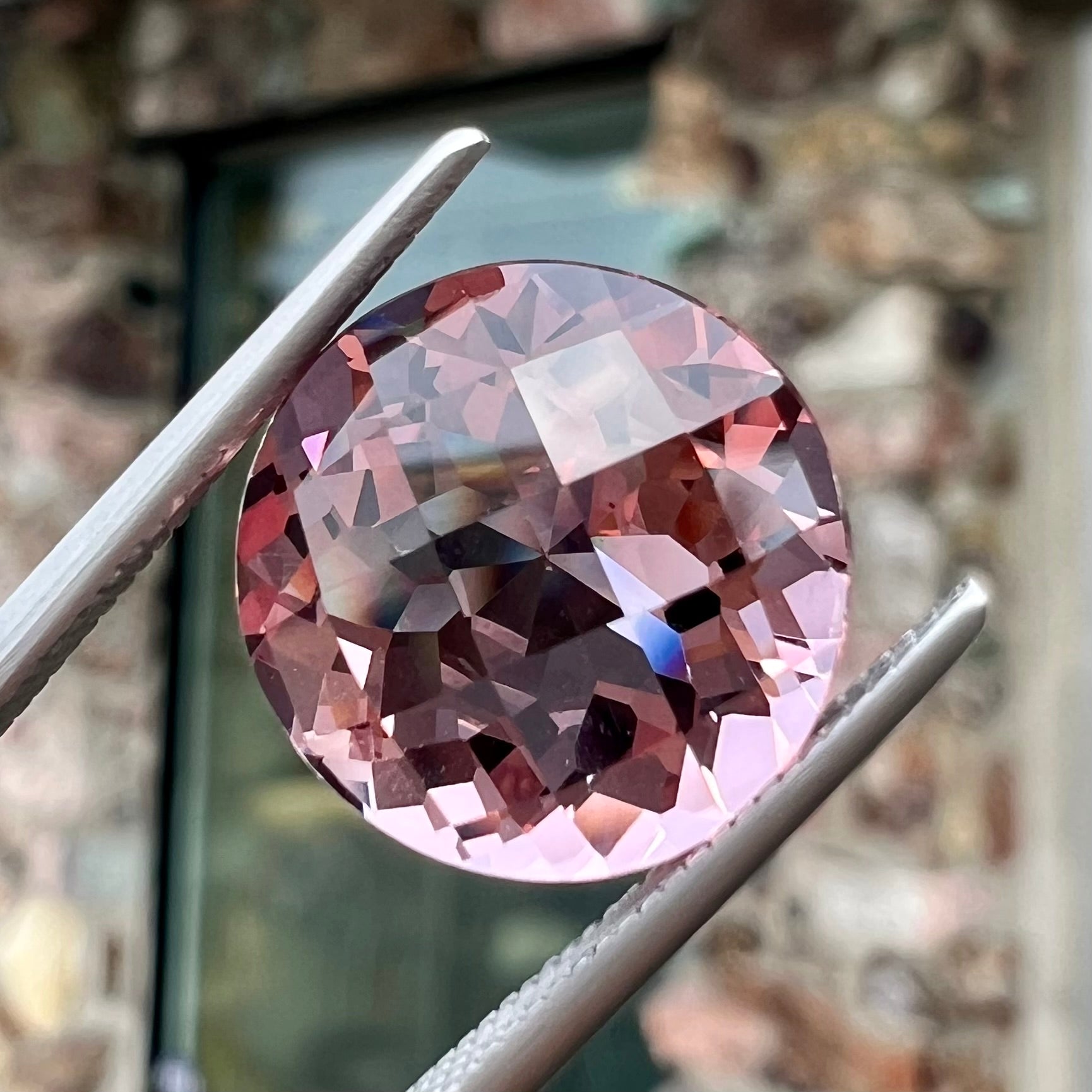 A loose, round brilliant checkerboard cut Zandrite gemstone.  The stone changes colors from greenish tan to purple.