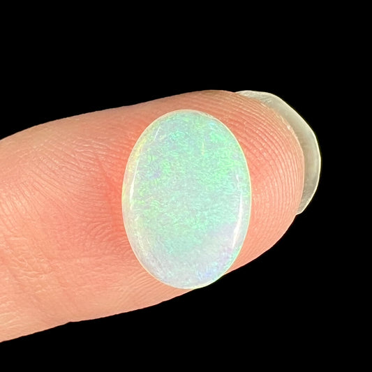 A loose, oval cabochon cut crystal opal from Coober Pedy, Australia.  The opal has green and blue colors.