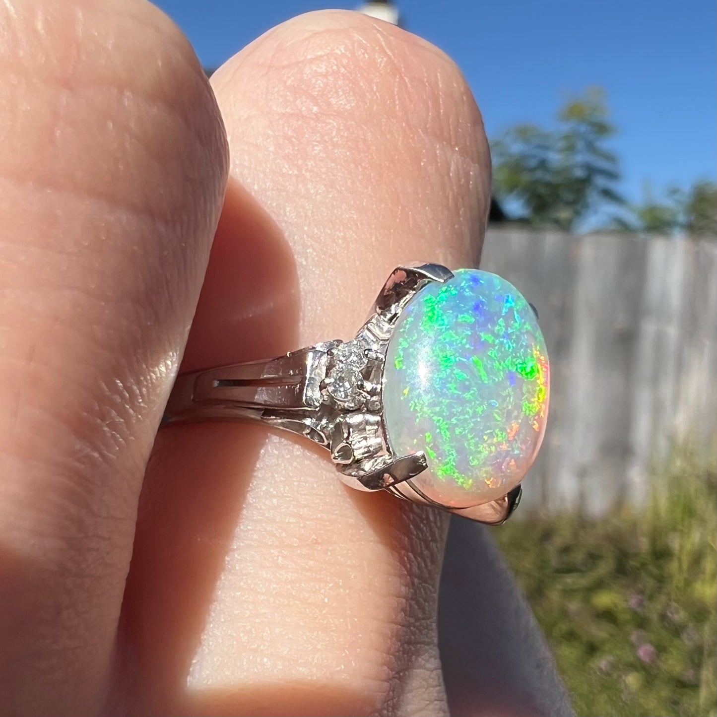 A platinum filigree opal engagement ring set with diamond accents.  The opal has green-blue colors.