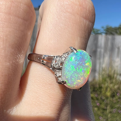 A platinum filigree opal engagement ring set with diamond accents.  The opal has green-blue colors.