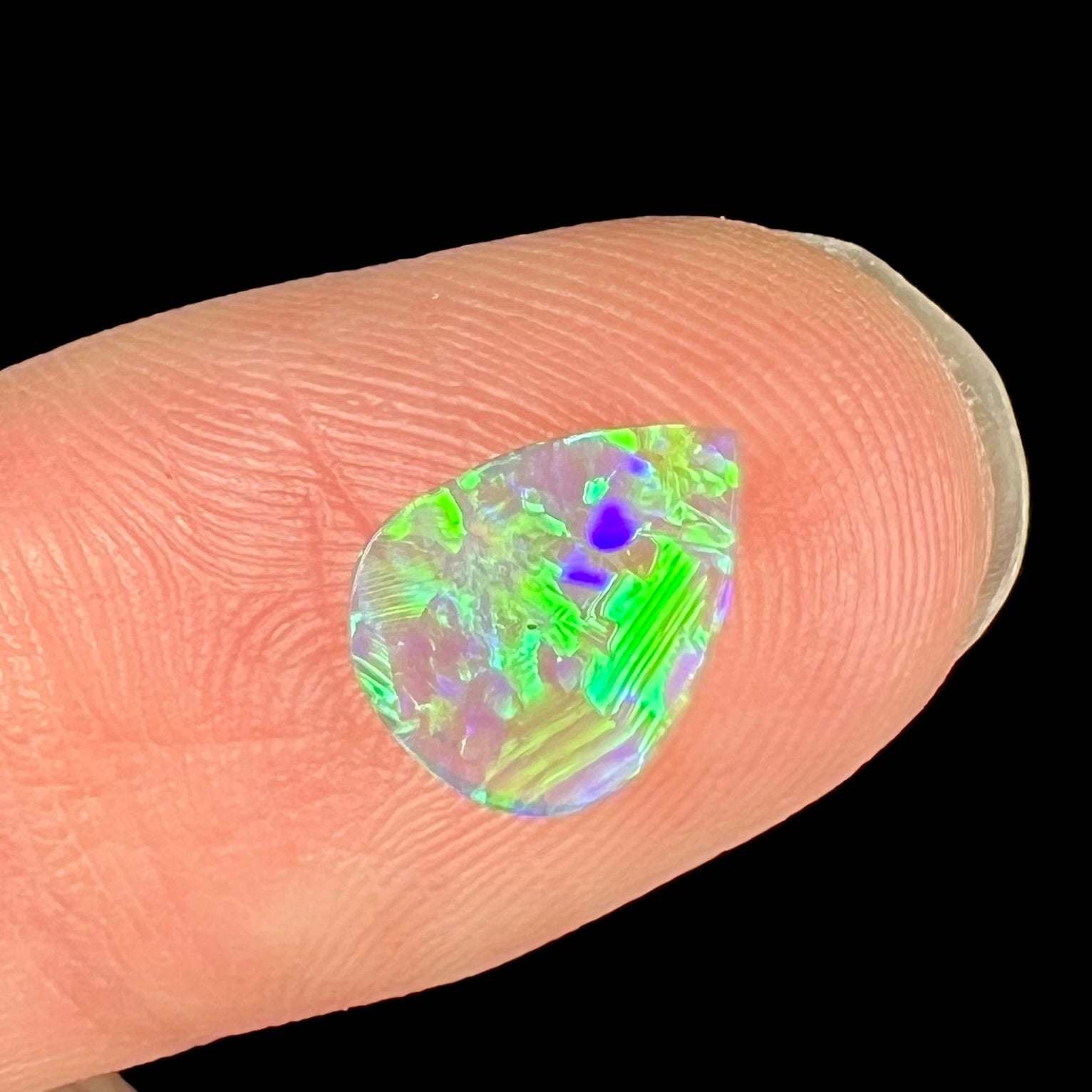 A loose pear shaped crystal opal with green and purple colors.