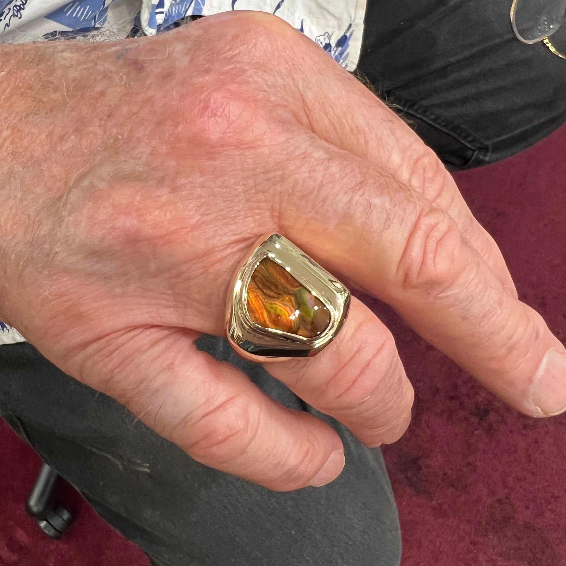 A heavy, yellow gold men's ring mounted with a Mexican fire agate stone.  The fire agate has orange, green, red, and purple colors.