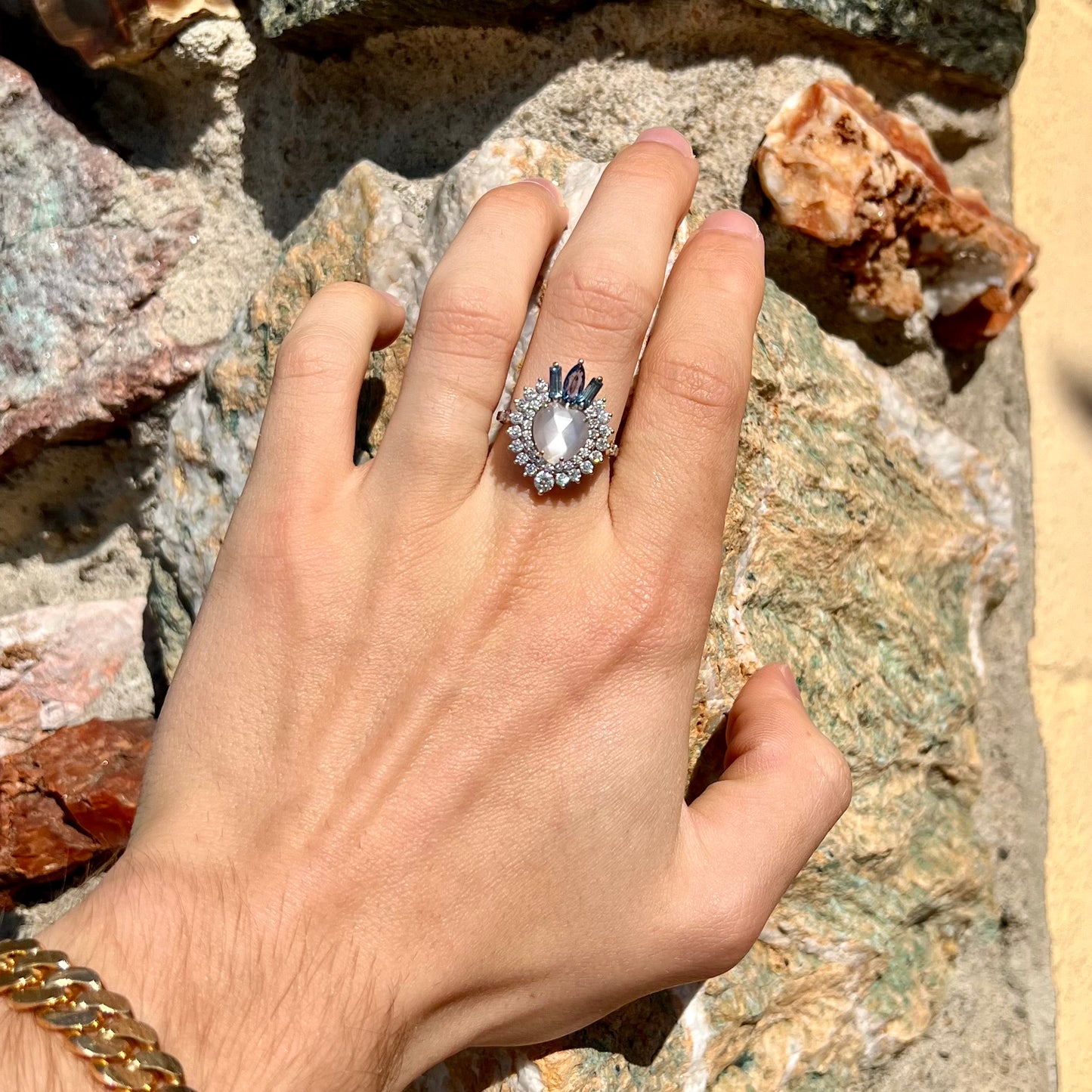 A ladies' white gold ring set with a faceted, heart shaped white moonstone, round moissanites, two aquamarine baguettes, and a marquise cut blue sapphire.