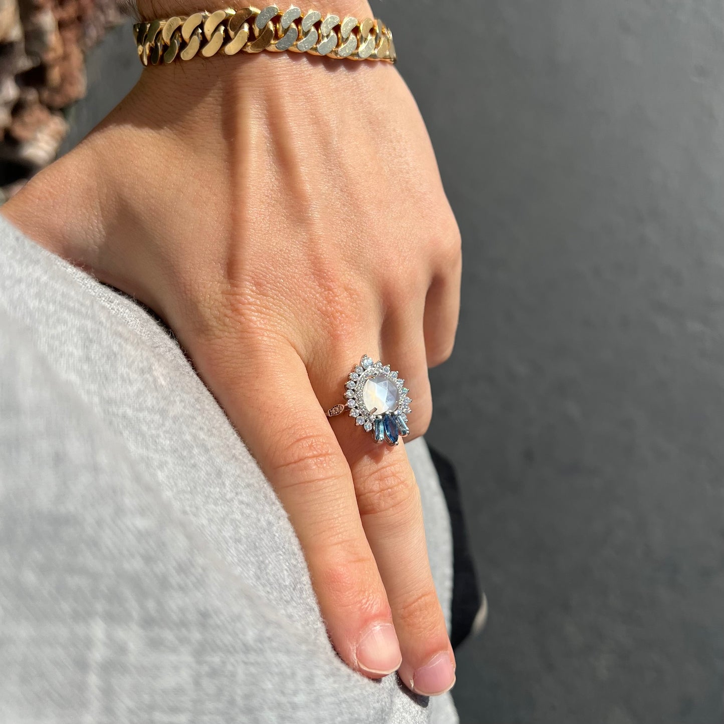 A ladies' white gold ring set with a faceted, heart shaped white moonstone, round moissanites, two aquamarine baguettes, and a marquise cut blue sapphire.