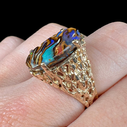 A yellow gold solitaire ring mounted with a Koroit boulder opal stone that shows the picture of a peacock.