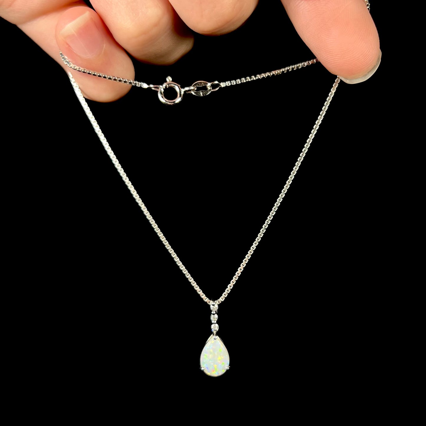 A platinum drop pendant mounted with three diamond accents and a pear shaped opal.