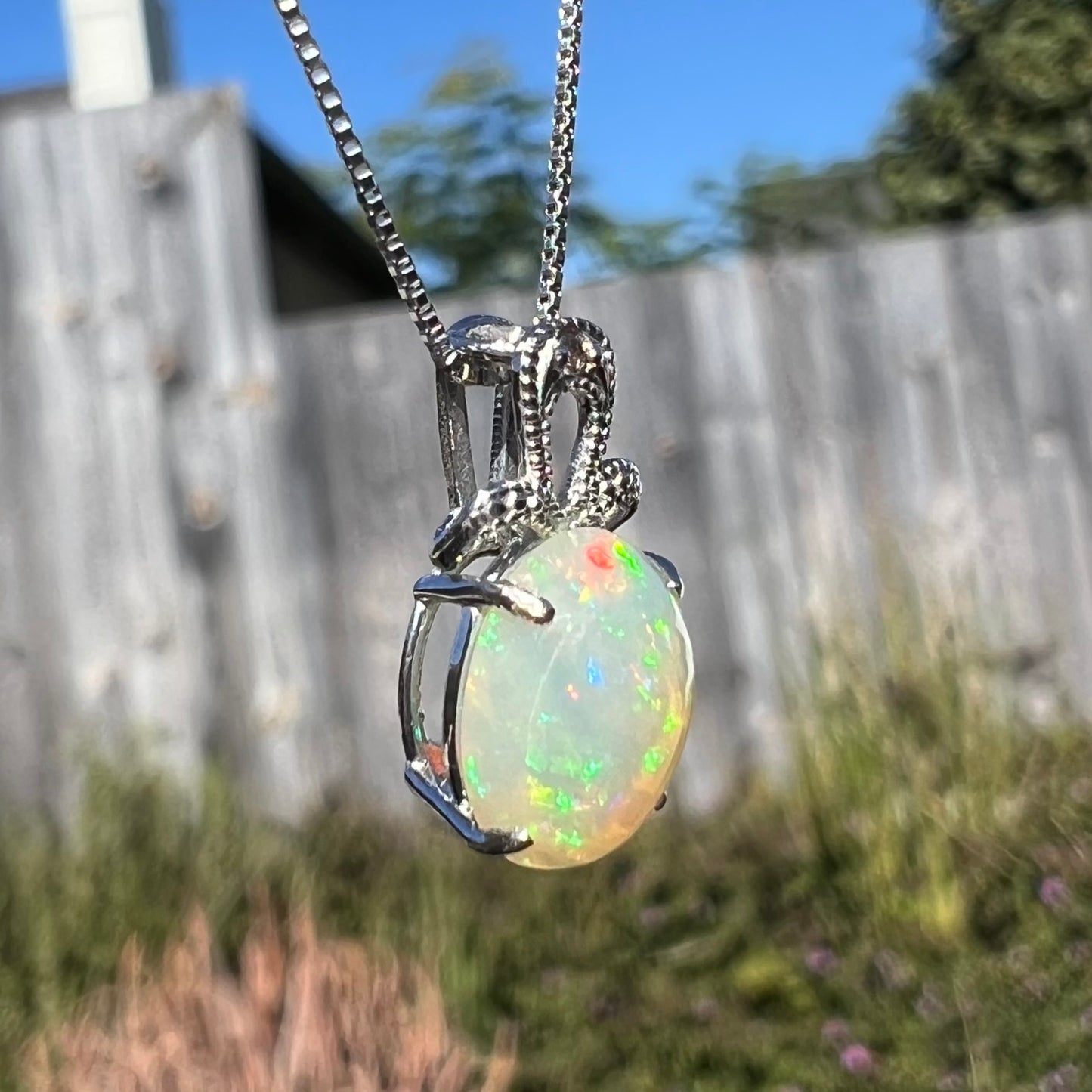 An oval cut Ethiopian opal mounted in a diamond-accented, 18 karat white gold pendant on a box chain.