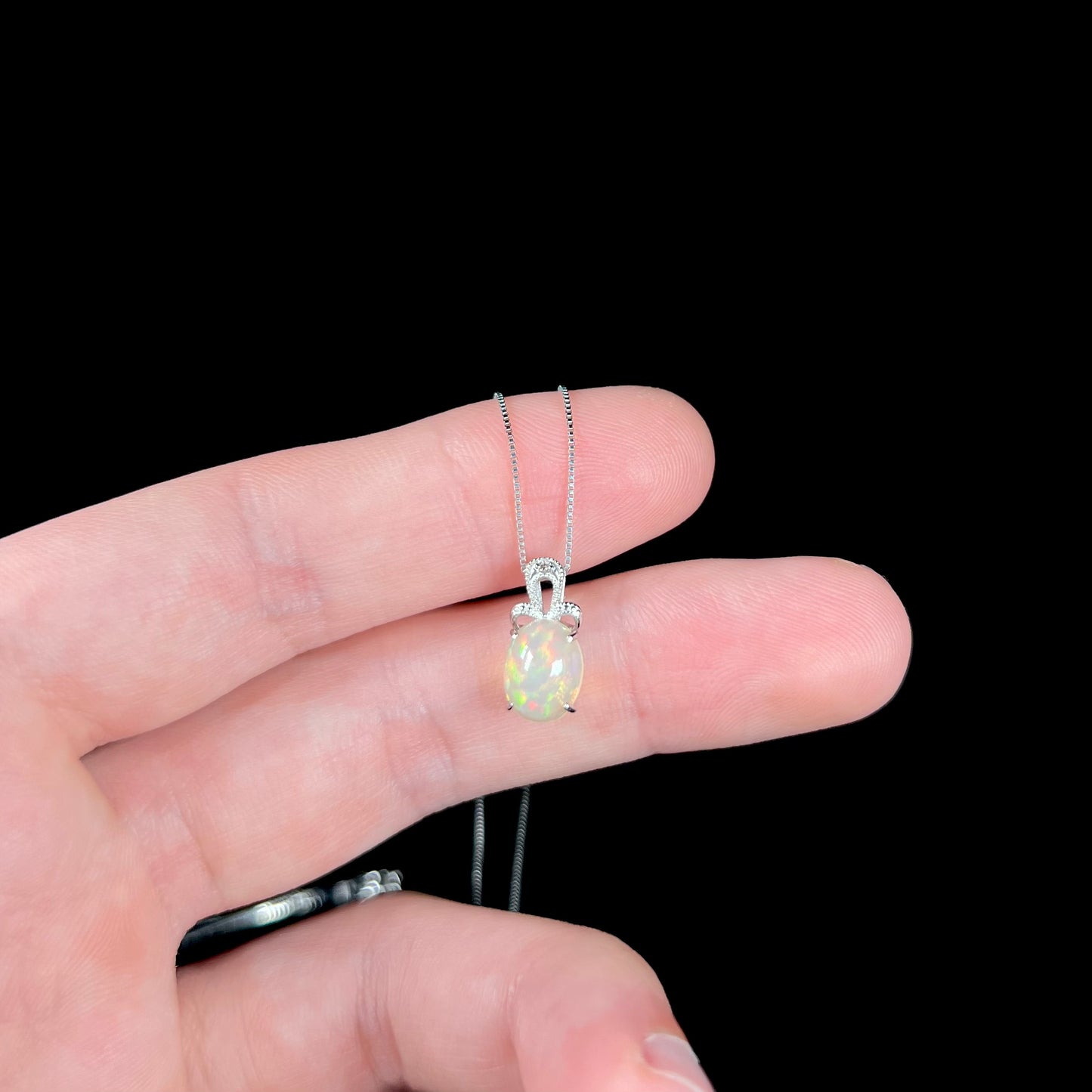 An oval cut Ethiopian opal mounted in a diamond-accented, 18 karat white gold pendant on a box chain.