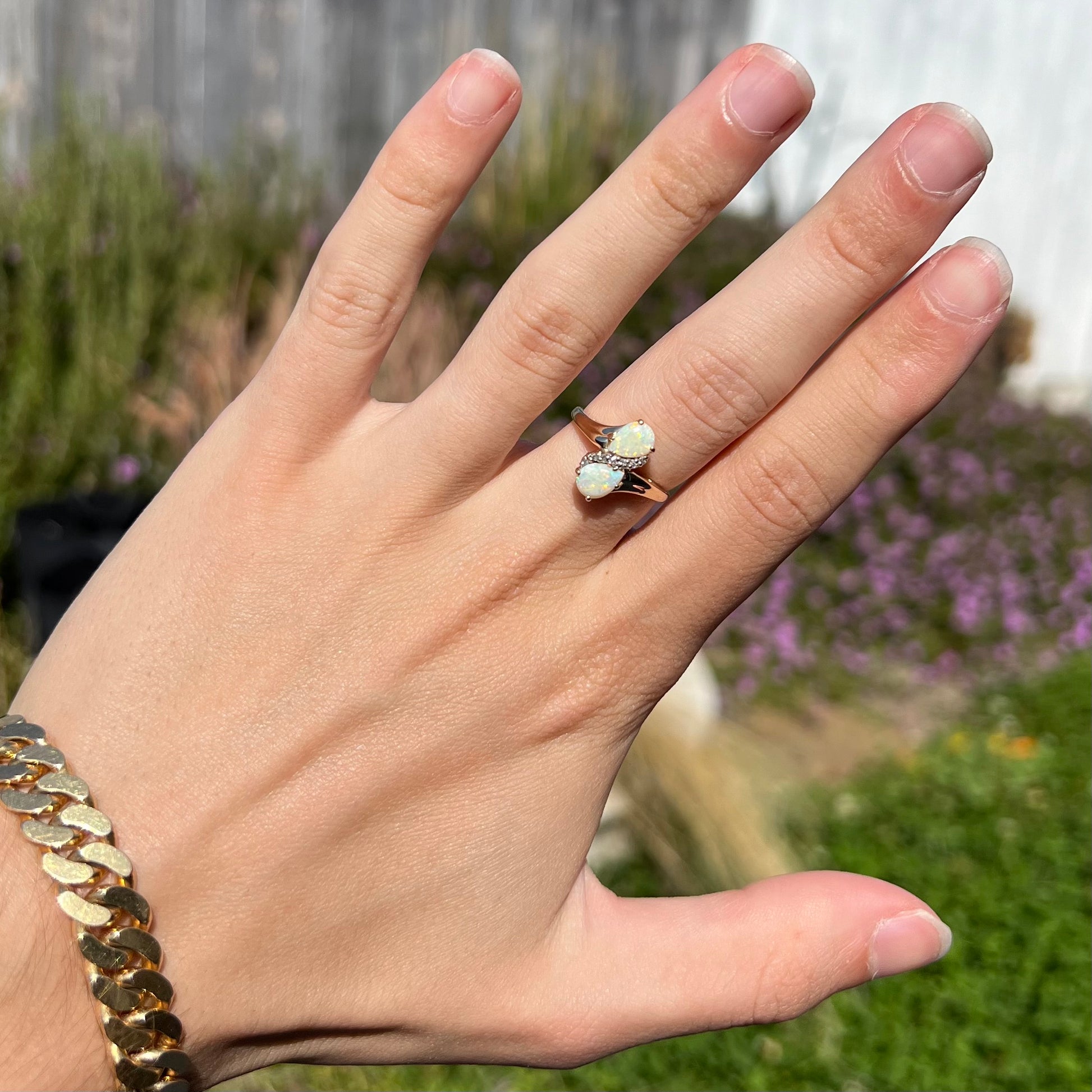 A yellow gold ring mounted with two pear shaped opals and diamond accents  The stones form an infinity shaped design.