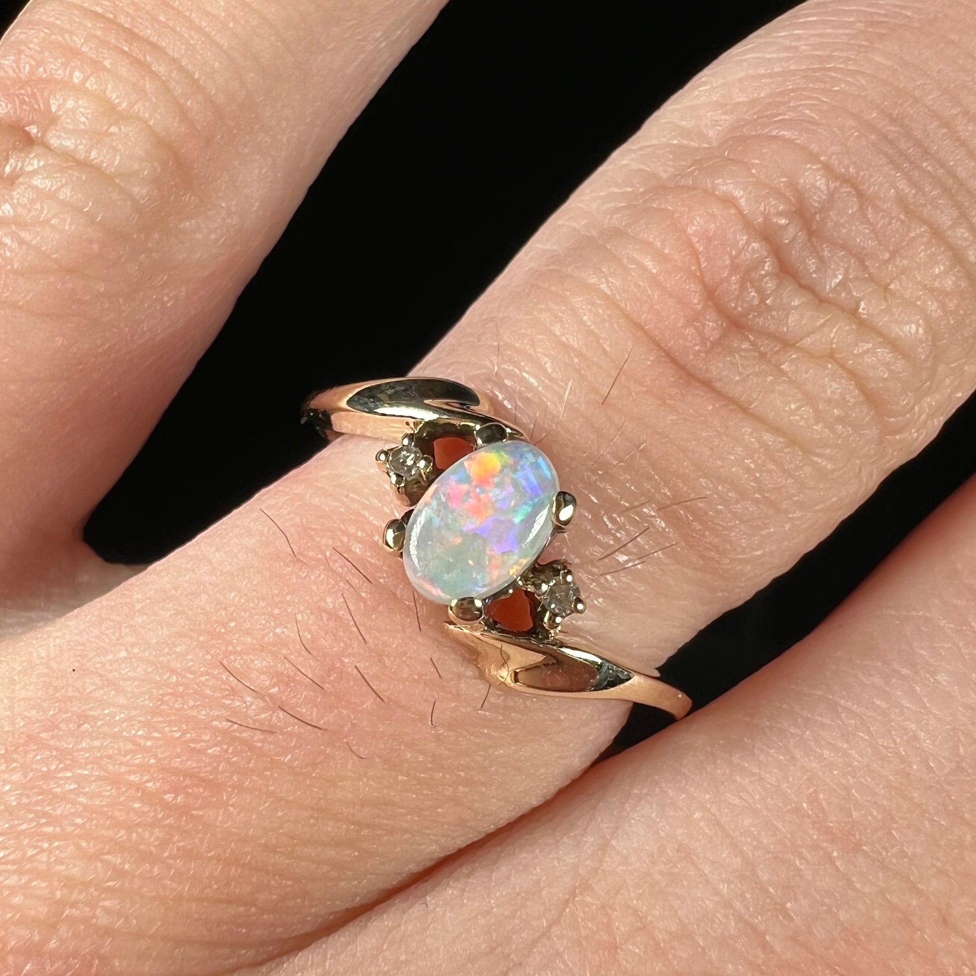 A dainty yellow gold opal and diamond-accented ring.  The opal has red and purple colors.