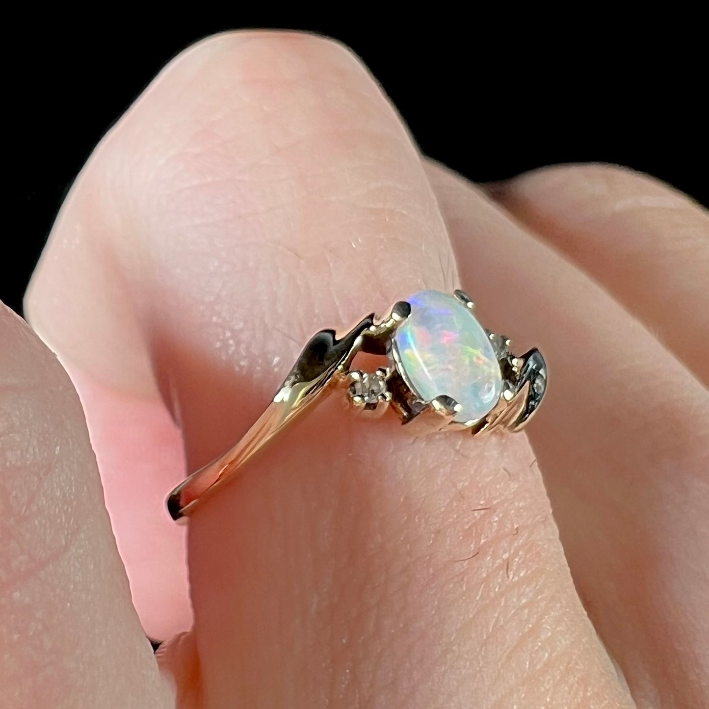 A dainty yellow gold opal and diamond-accented ring.  The opal has red and purple colors.