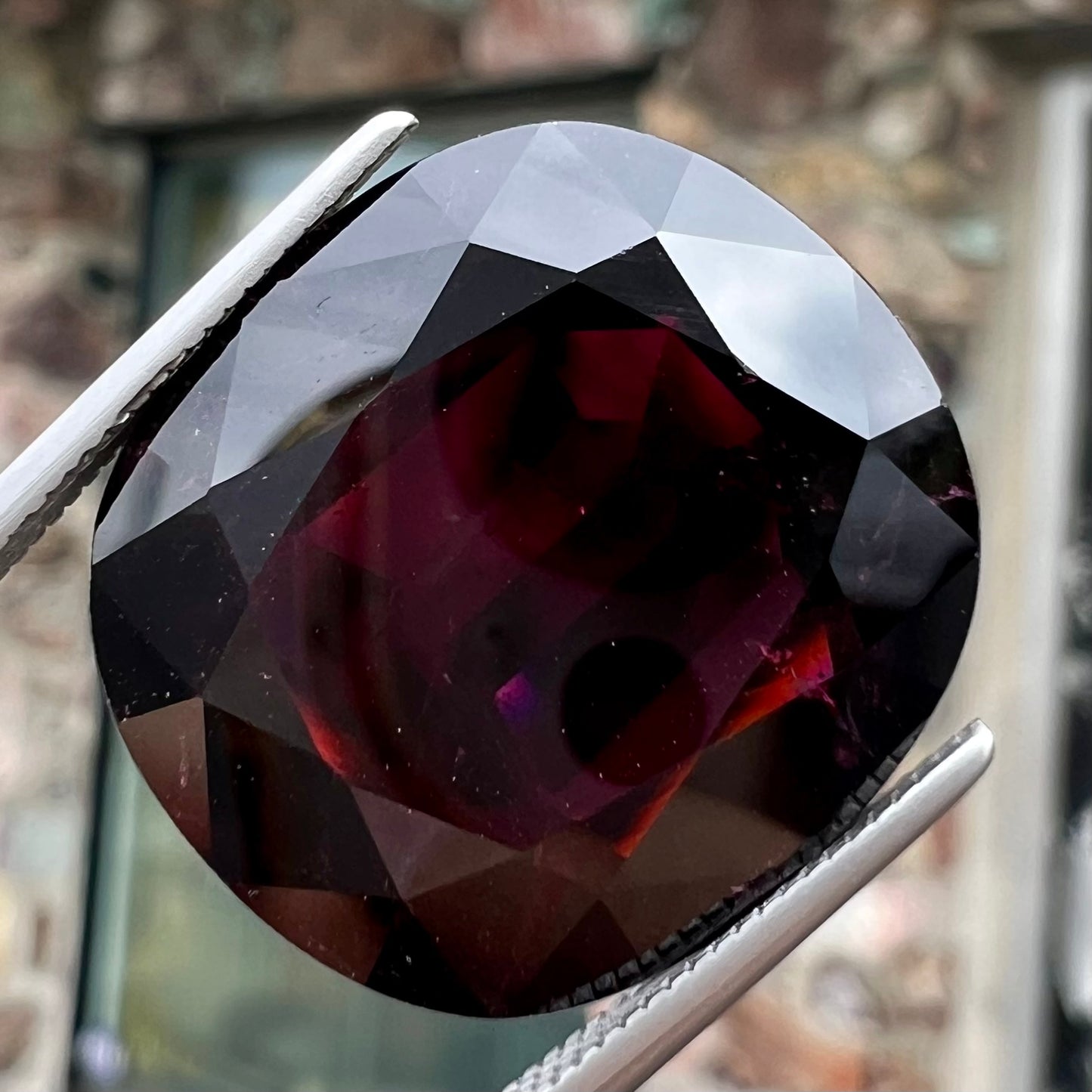 A loose, faceted oval cut rubellite tourmaline gemstone.  The stone is a dark purple red color.