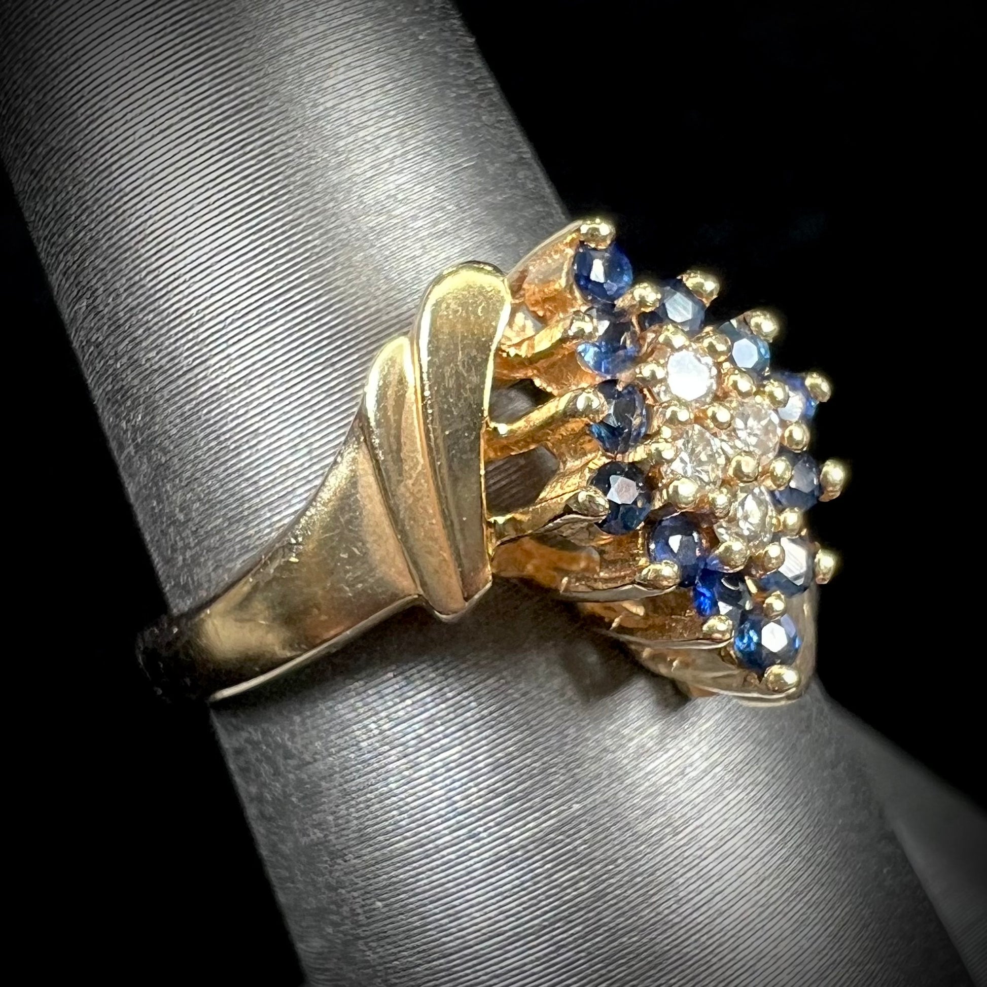 An estate, yellow gold ladies' cluster ring mounted with four round diamonds and twelve round blue sapphires.