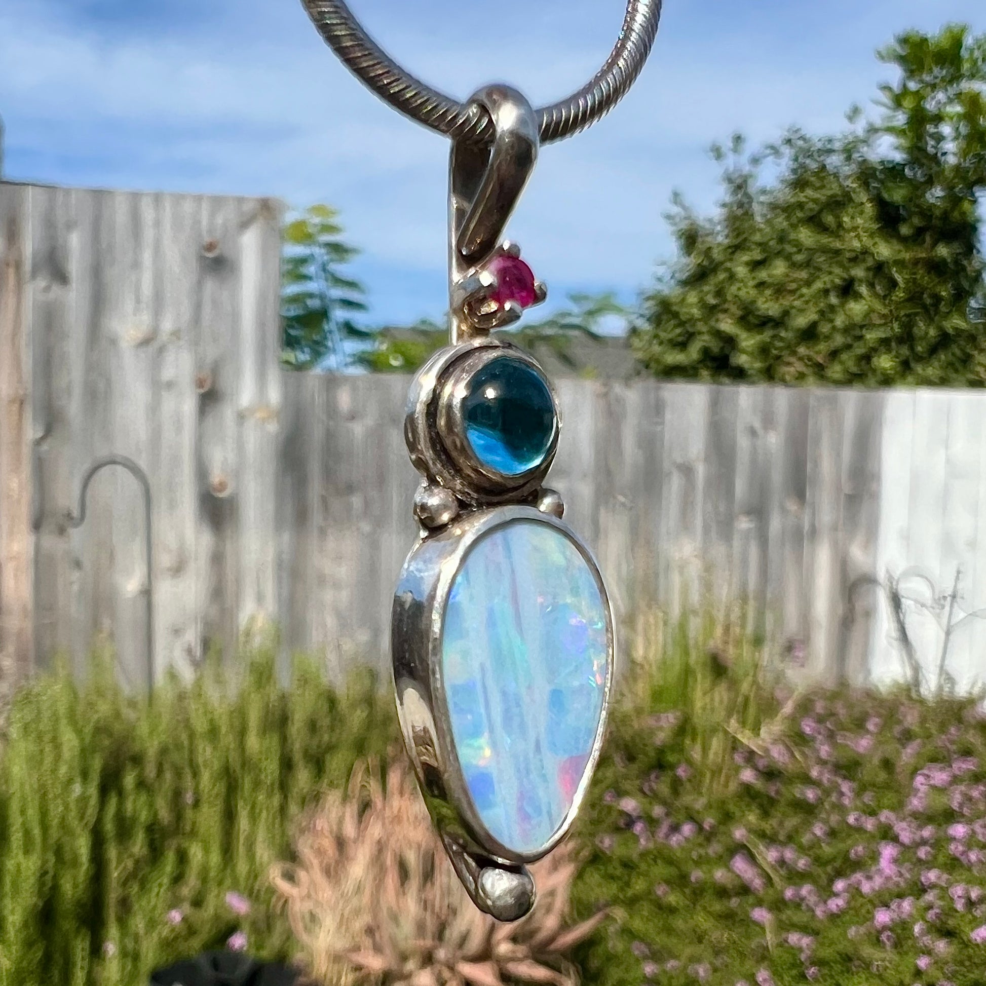 A sterling silver necklace shaped like a child, mounted with an opal doublet, a ruby, and a blue piece of glass.