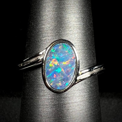 A sterling silver ring bezel-set with an oval shaped black opal doublet.  The opal has red and blue fire.