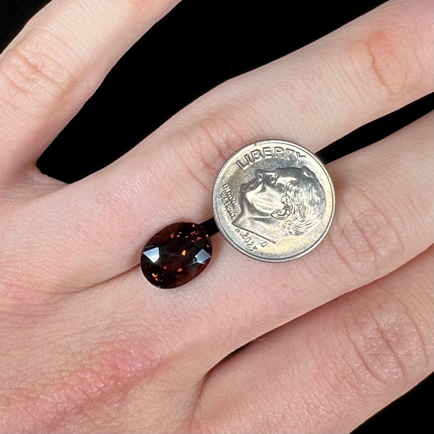 A loose, faceted oval cut dravite tourmaline gemstone.  The stone is a dark brown color with a purple secondary color.