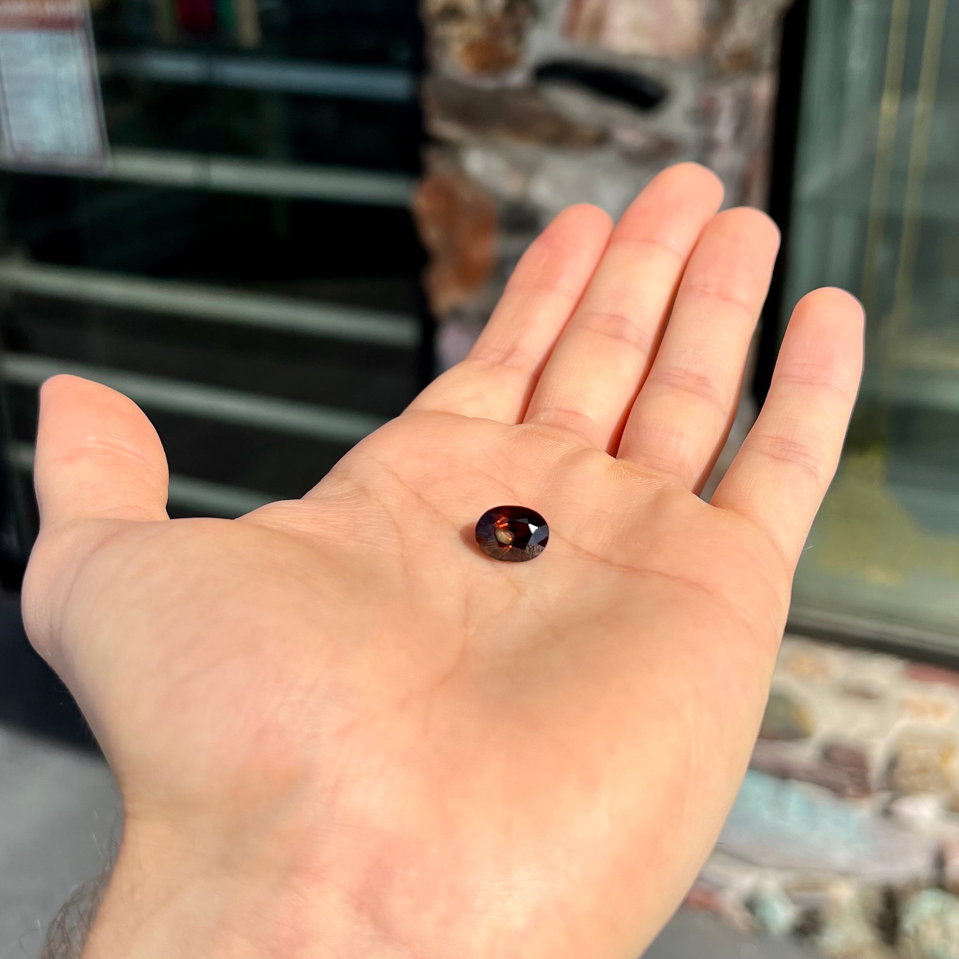 A loose, faceted oval cut dravite tourmaline gemstone.  The stone is a dark brown color with a purple secondary color.