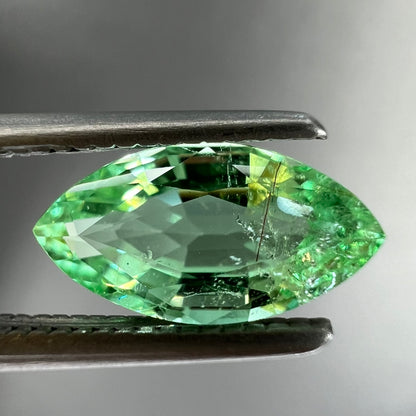 A faceted marquise cut electric green tourmaline gemstone.  The stone has an eye-visible rutile needle inclusion.