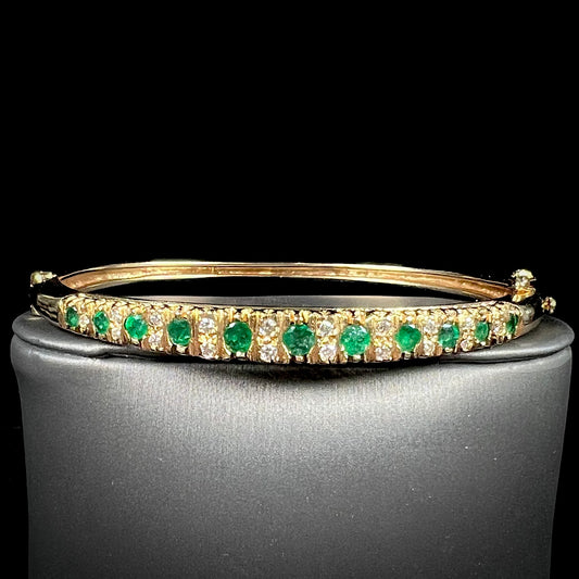 A ladies' yellow gold bangle bracelet set with round cut emeralds and diamonds.