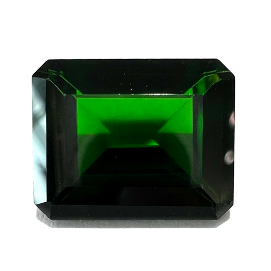 A large, emerald cut chrome diopside gemstone.  The gem is dark green color.