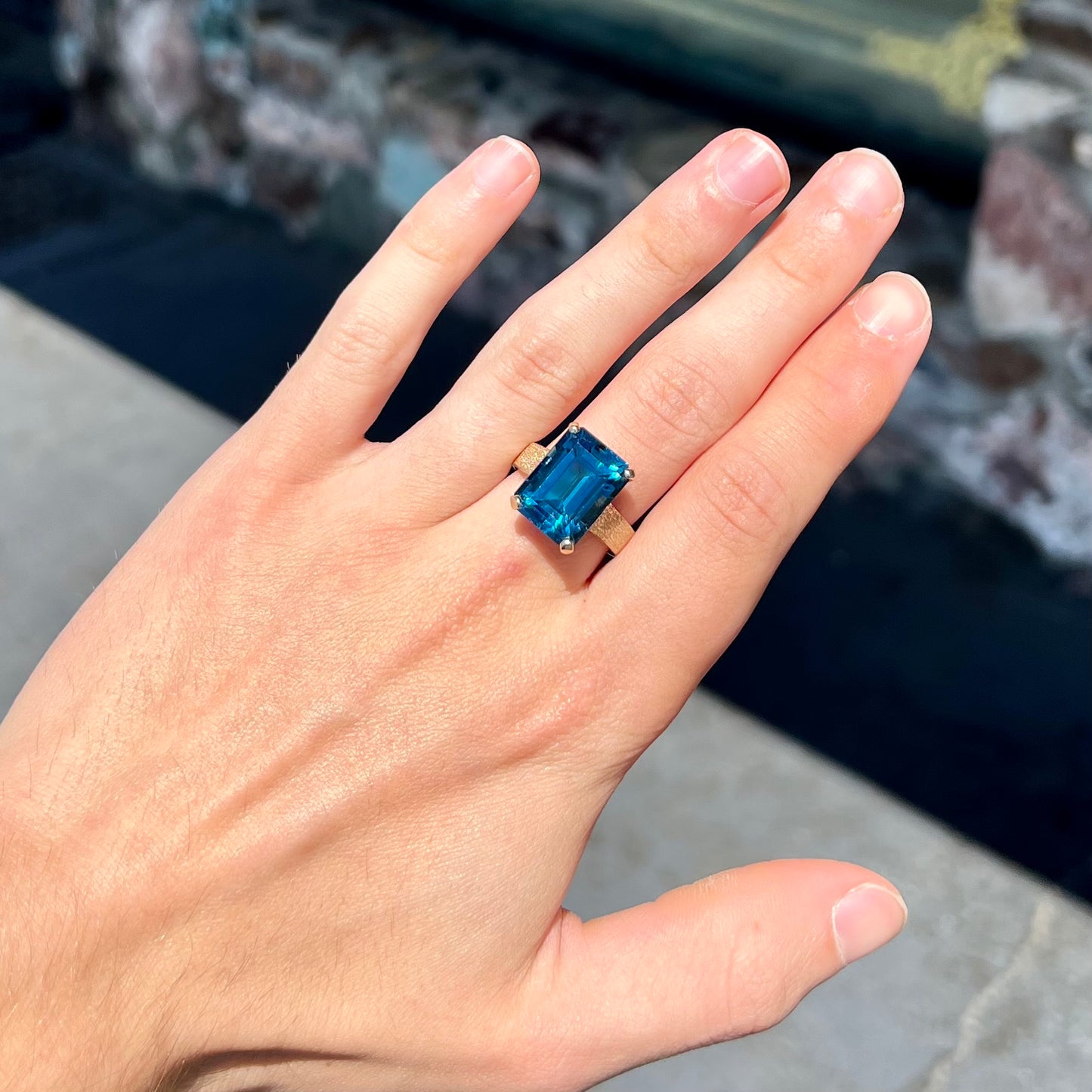 A ladies' yellow gold London blue topaz solitaire ring.  The ring is textured, and the topaz is emerald cut.