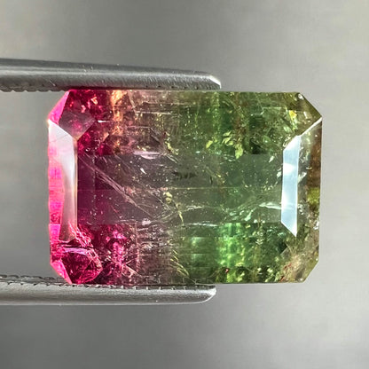 A loose watermelon tourmaline gemstone.  The stone is emerald cut and fades from hot pink to green.