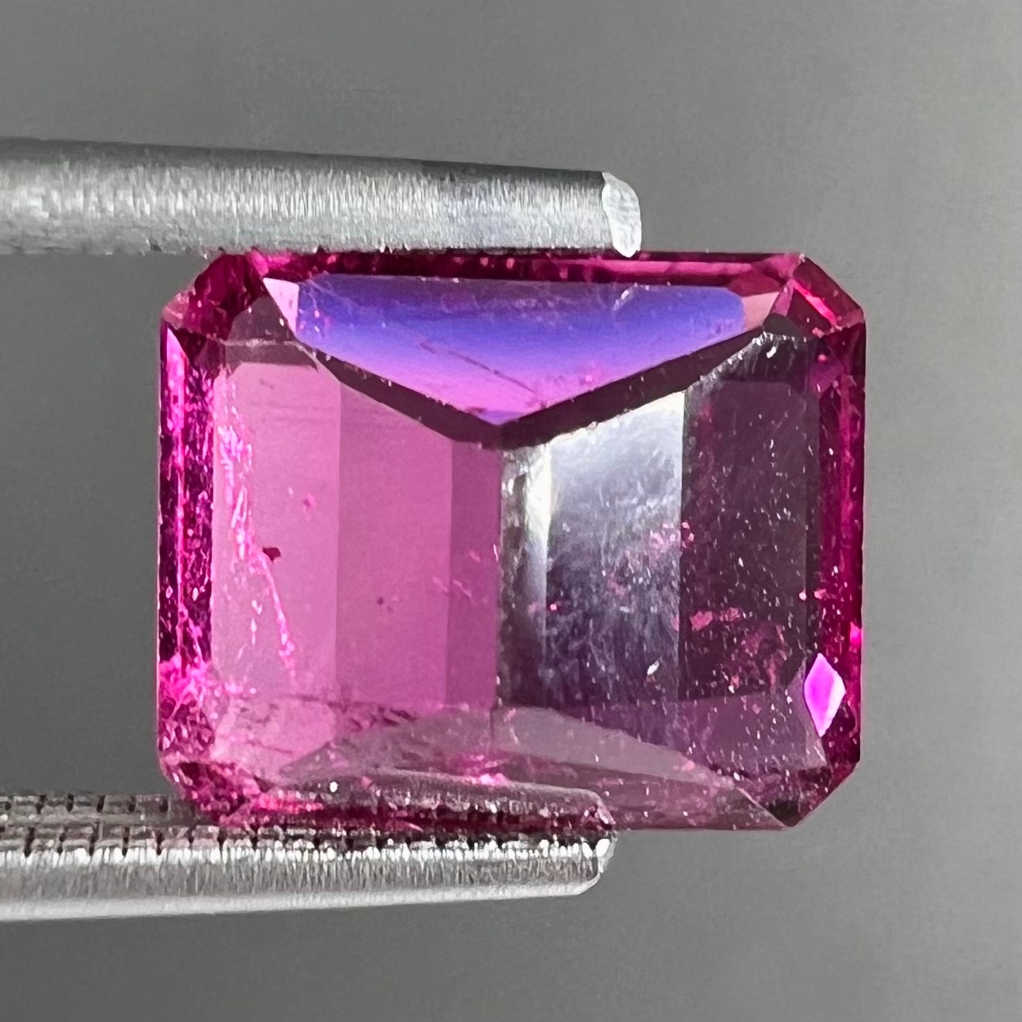 A loose, faceted modified emerald cut hot pink tourmaline stone.