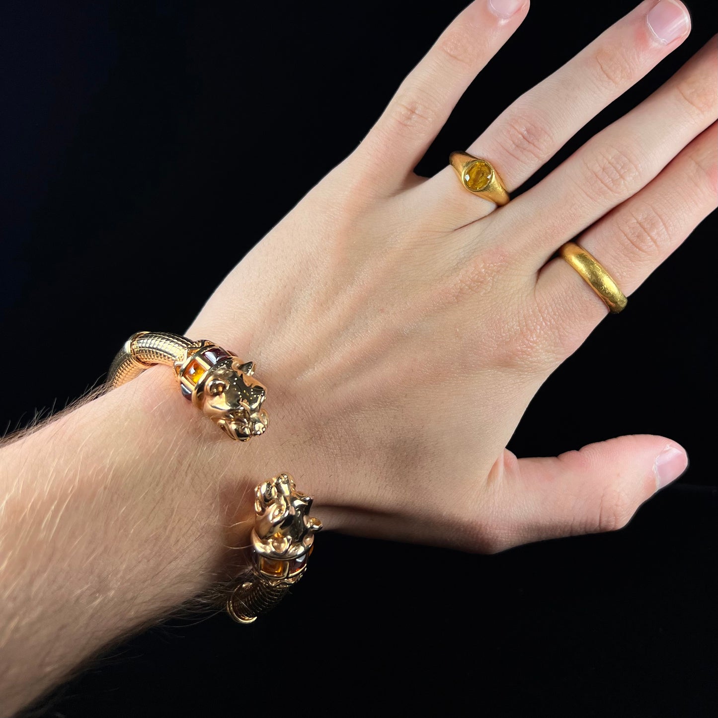 A 14 karat yellow gold hinged bangle bracelet featuring the motif of two panther heads.  There are yellow and red accent stones.