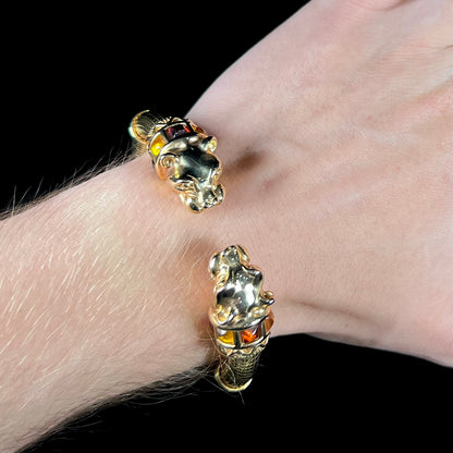 A 14 karat yellow gold hinged bangle bracelet featuring the motif of two panther heads.  There are yellow and red accent stones.