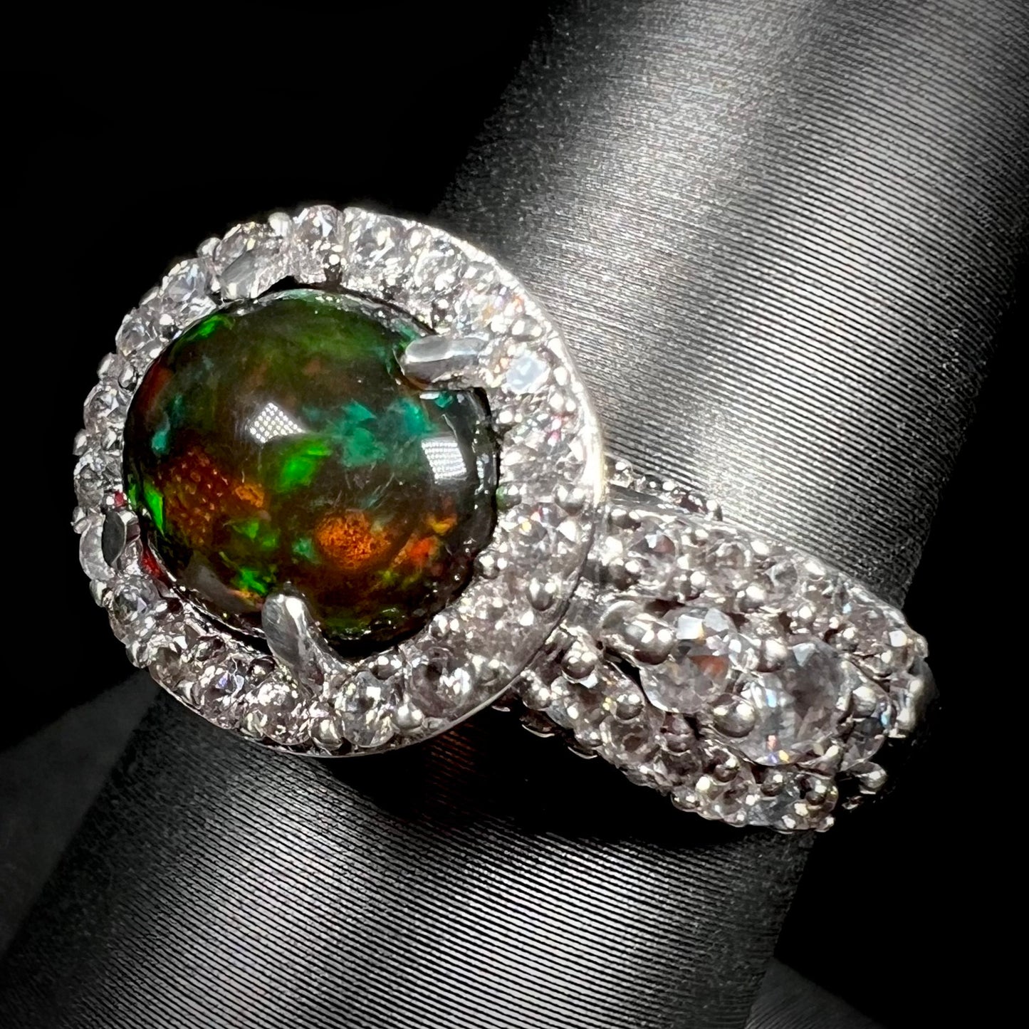 A CZ-accented sterling silver halo ring mounted with a smoked Ethiopian fire opal.  The opal plays green, red, and blue colors.