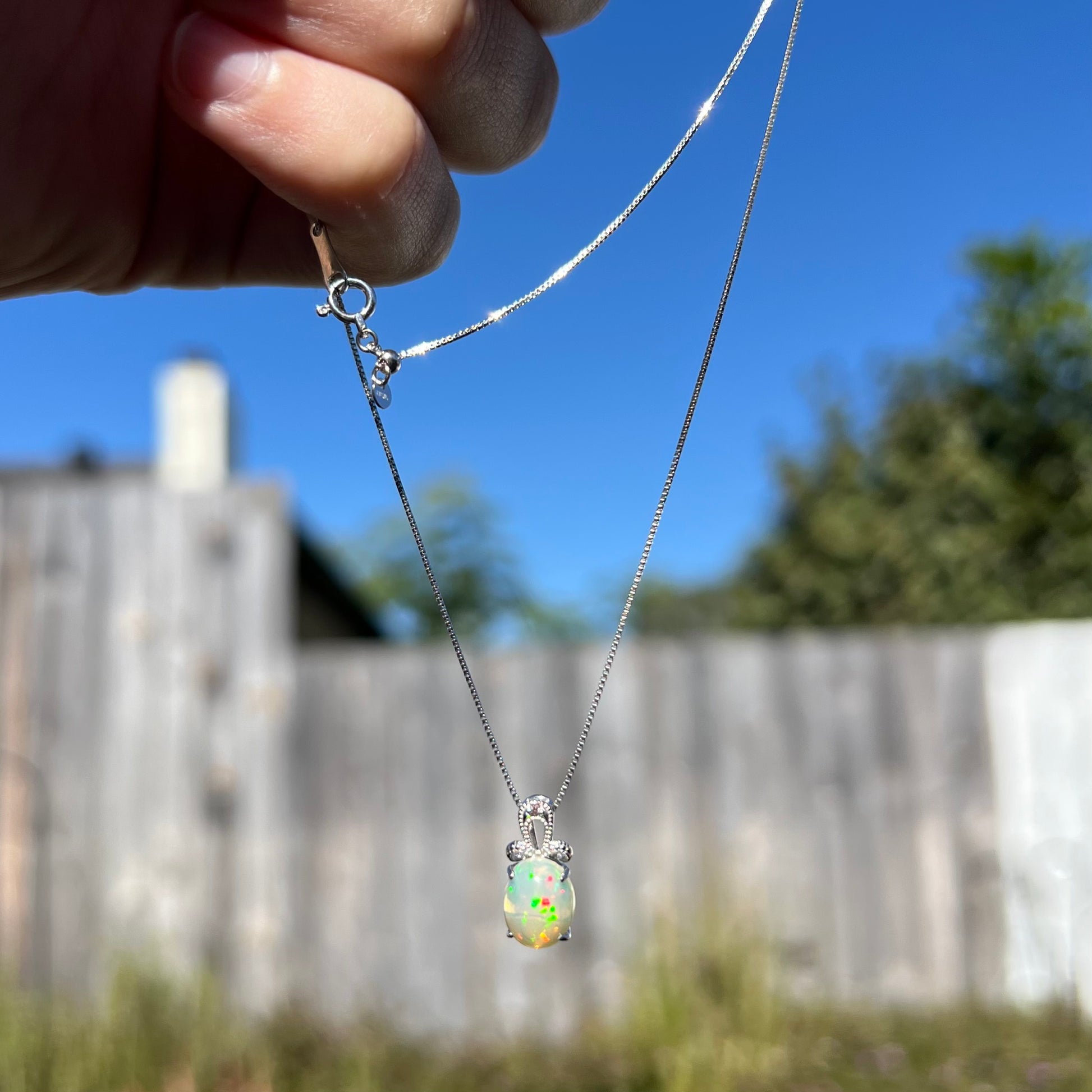 An oval cut Ethiopian opal mounted in a diamond-accented, 18 karat white gold pendant on a box chain.