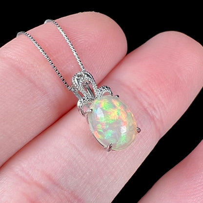 An oval cut Ethiopian opal mounted in a diamond-accented, 18 karat white gold pendant on a box chain.