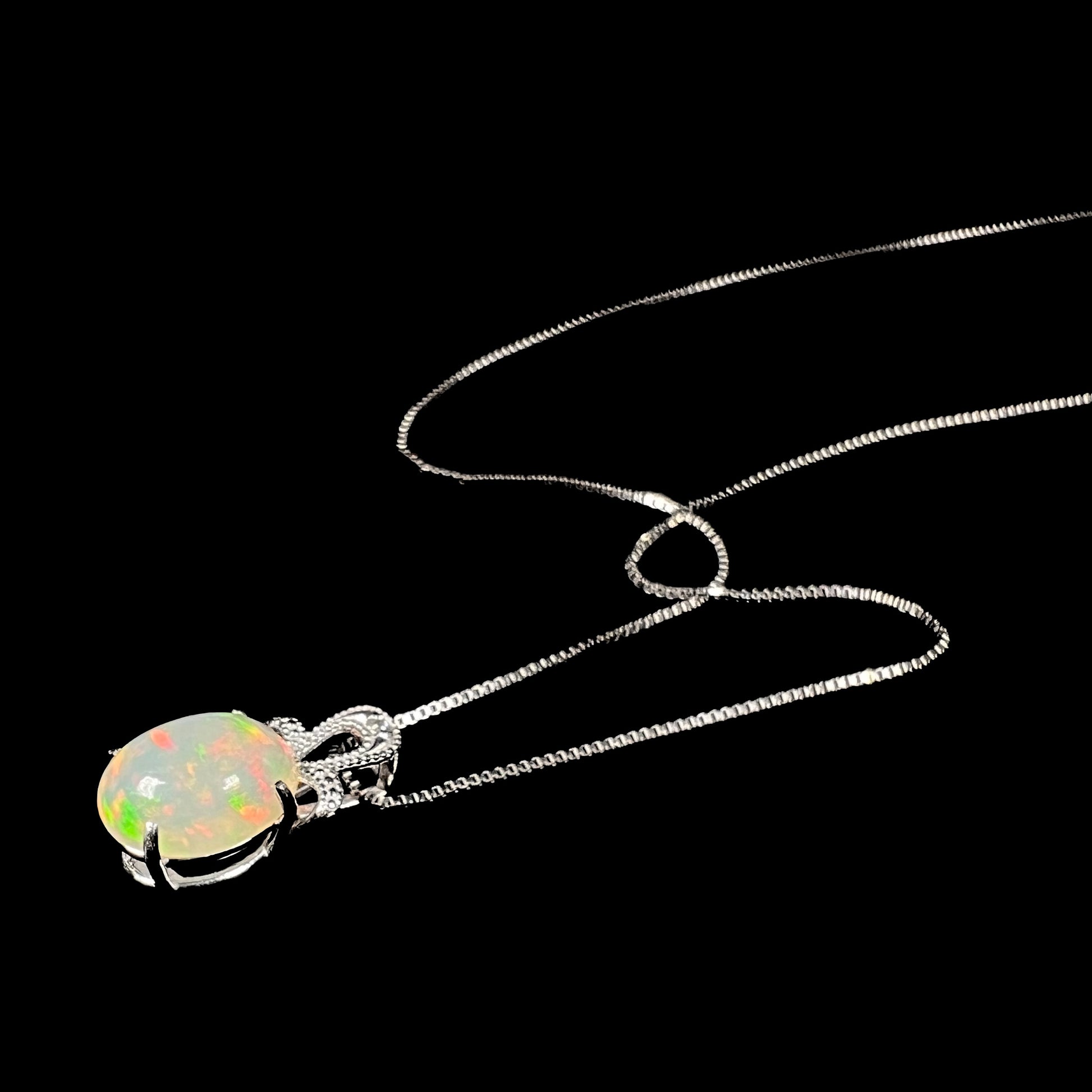 An oval cut Ethiopian opal mounted in a diamond-accented, 18 karat white gold pendant on a box chain.