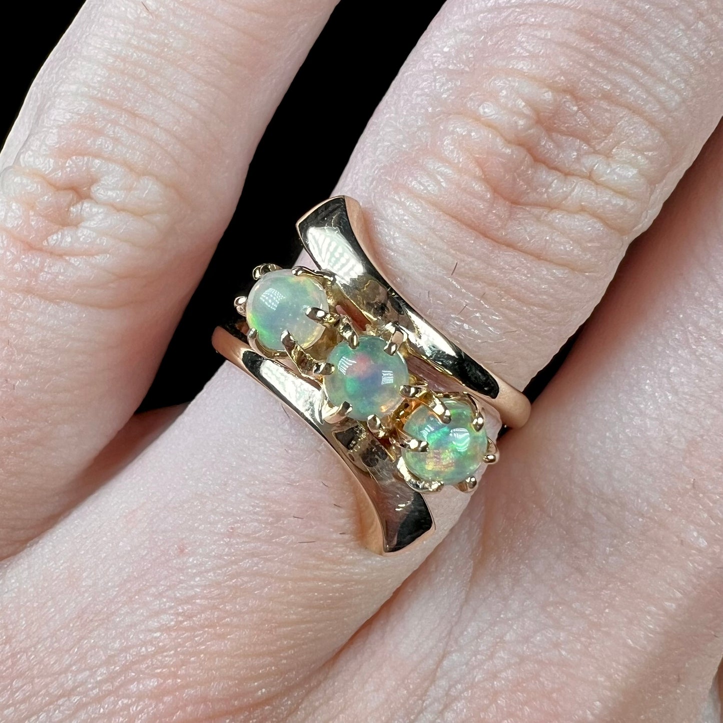 A yellow gold bypass shank ring mounted with three round cabochon cut Ethiopian fire opals.