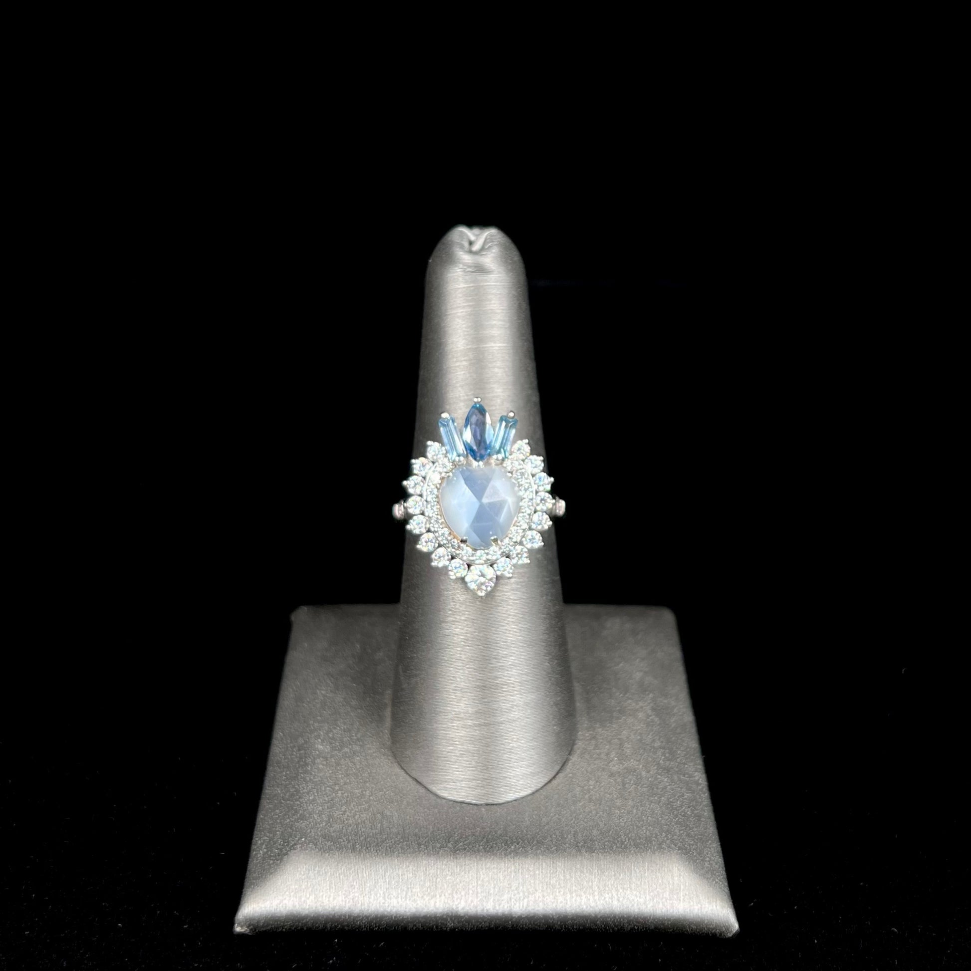 A ladies' white gold ring set with a faceted, heart shaped white moonstone, round moissanites, two aquamarine baguettes, and a marquise cut blue sapphire.