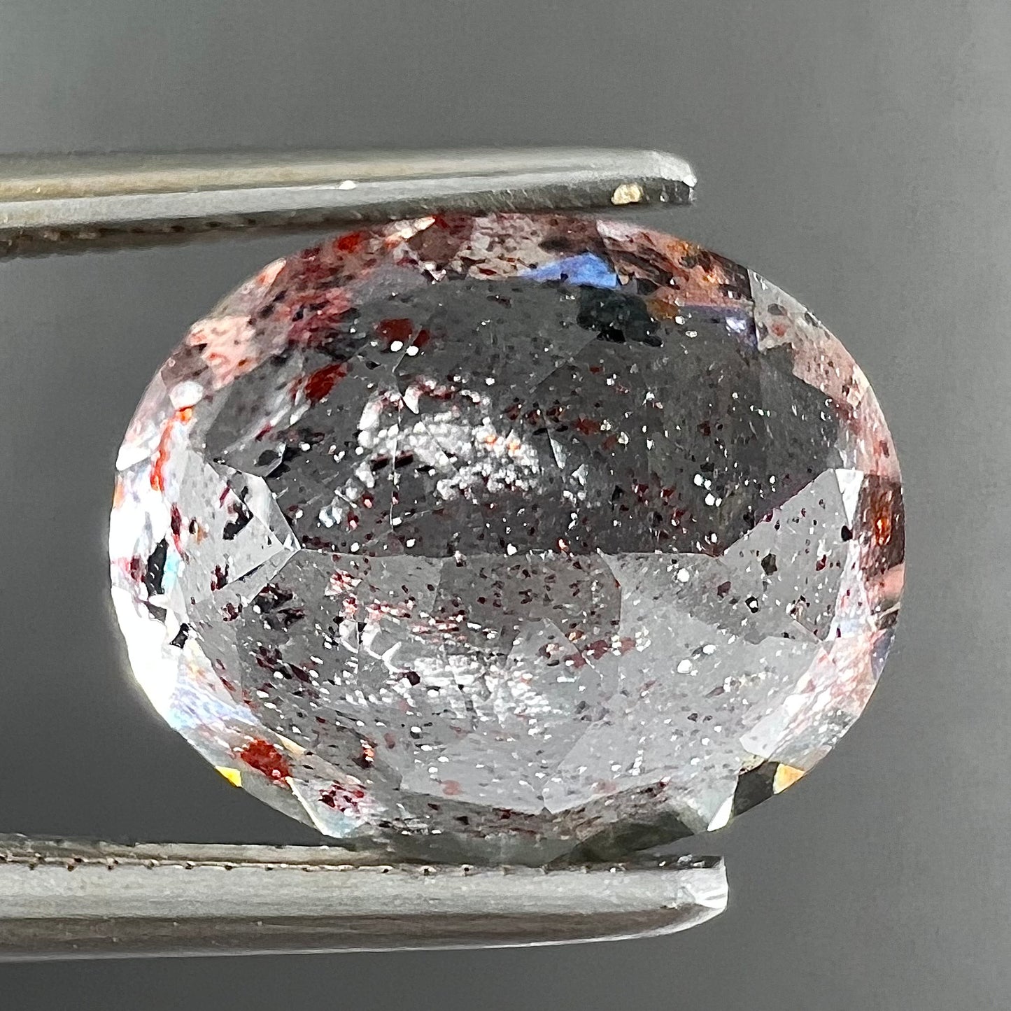 A loose, faceted oval cut lepidocrocite quartz stone.  The stone has red and black inclusions.