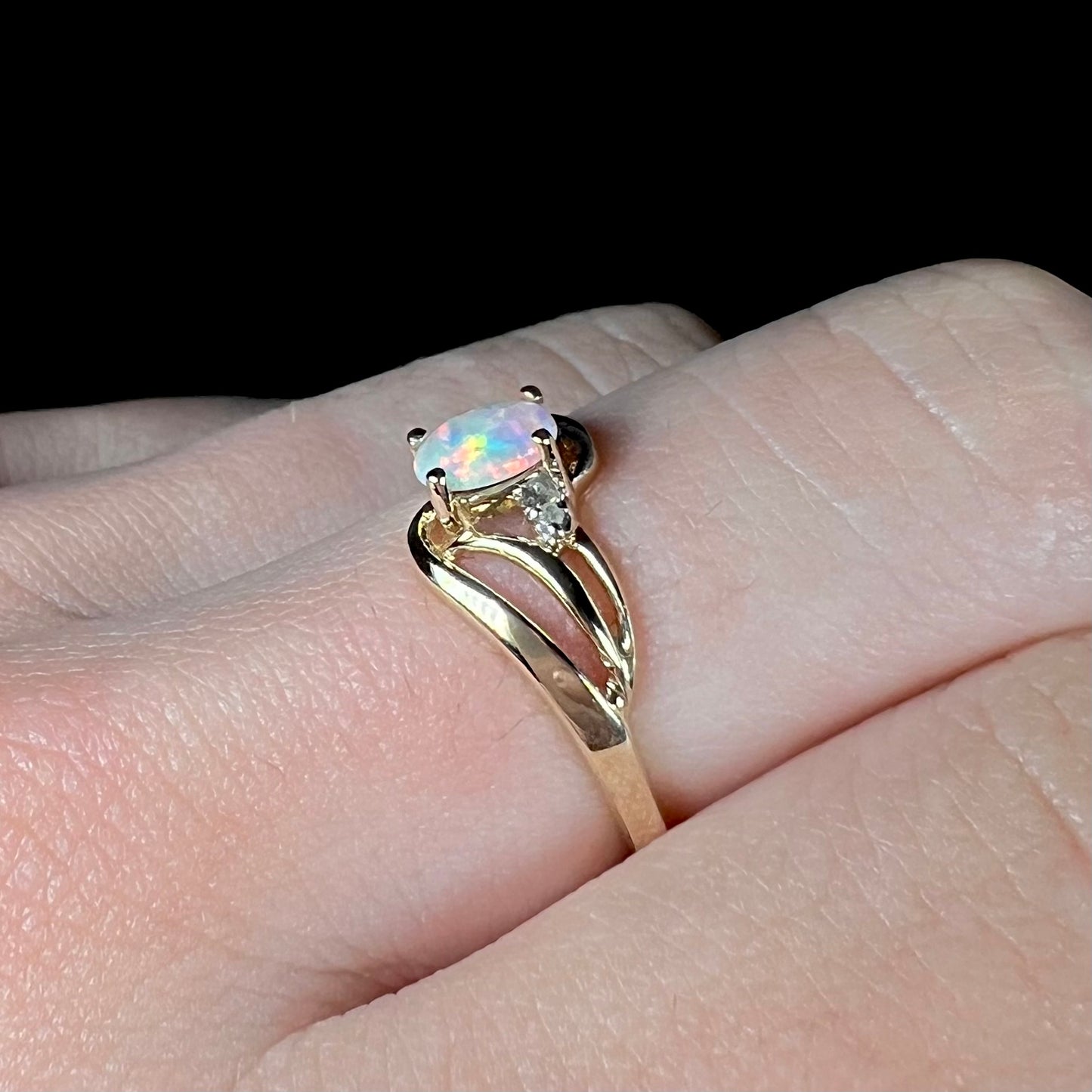 A yellow gold ring mounted with two diamond accents and an oval cut lab created opal.  The opal has bright red colors.