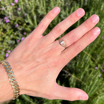 A yellow gold ring mounted with two diamond accents and an oval cut lab created opal.  The opal has bright red colors.