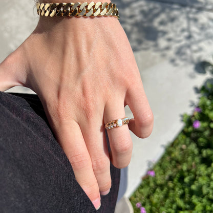 A yellow gold ring featuring two crossing, alternating lines of round cut synthetic opals.  In the middle is a larger oval cut synthetic opal.